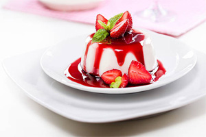 Panna Cotta mold drizzled with strawberry sauce and fresh strawberries