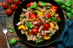 Cork-screw past topped with red and yellow bellpeppers, tomatoes, spinach, and basil